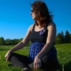 This is a picture of a pregnant lady sitting crossed legged in a field on a sunny day.